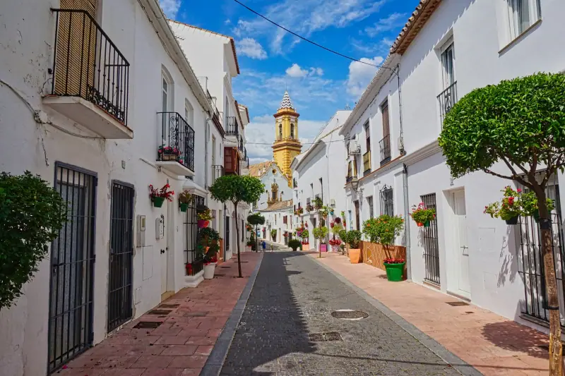 Whitewashed street with flower pots in Estepona old town, the church tower behind